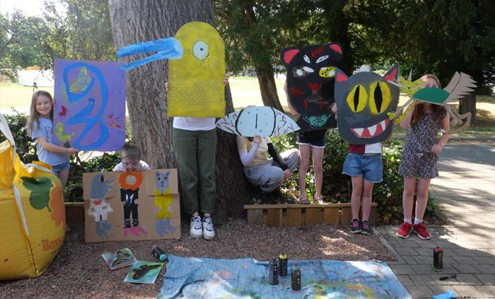 Children posed as part of their artworks, large scale brightly coloured drawings on cardboard. Creating a collaged scene of animals with their painted